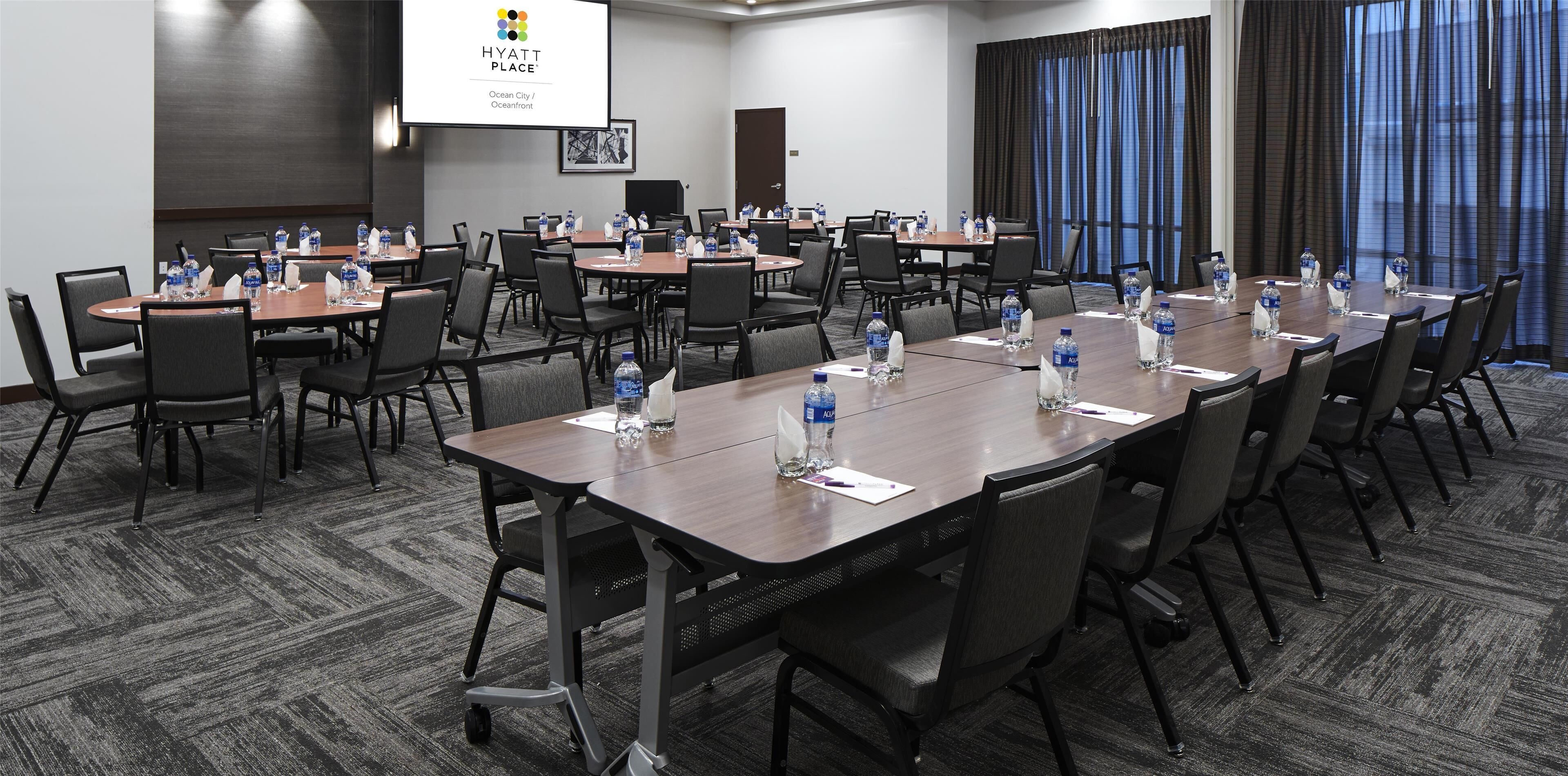 Un salón de conferencias con varias mesas, sillas y botellas de agua.
