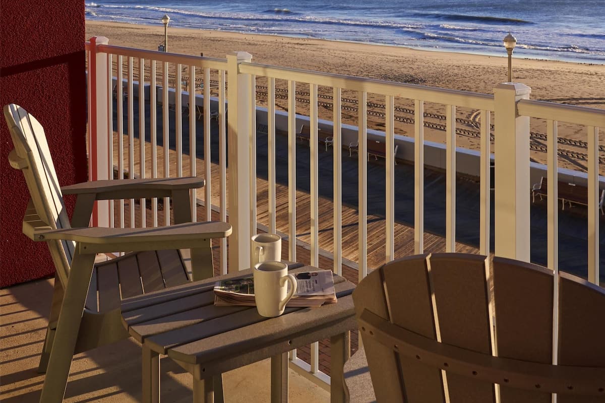 A wooden deck with two Adirondack chairs and a table, overlooking a beach with a railing.