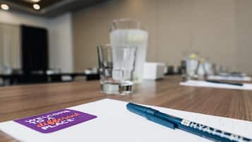 A hotel conference room with a wooden table, a glass of water, a notepad, and a pen.
