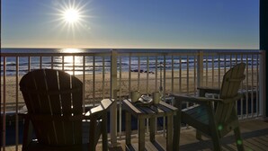 Une terrasse avec deux fauteuils Adirondack et une petite table, donnant sur une plage avec l’océan et un ciel dégagé.