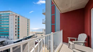 Un balcon avec un mur rouge, une balustrade blanche et un fauteuil Adirondack blanc.