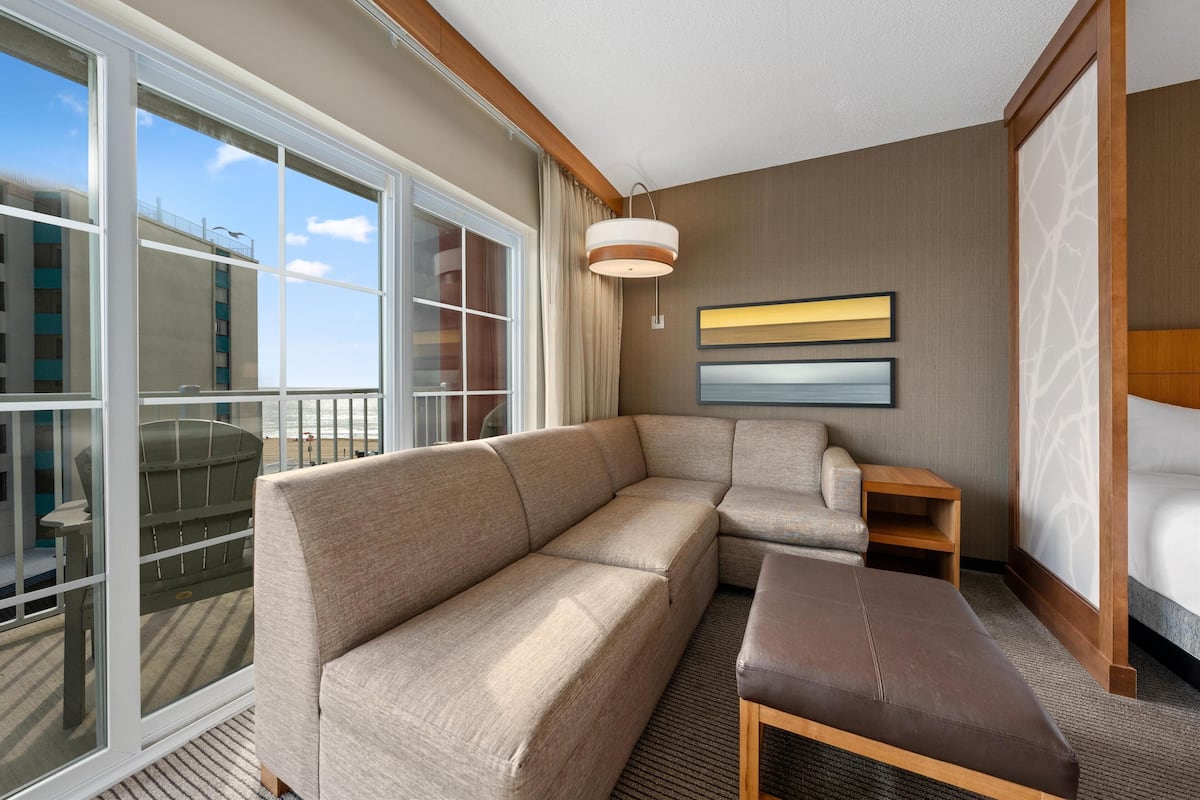 A modern hotel room with a large window, a sofa, a chair, and a bed.