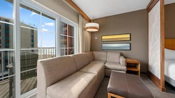 A modern hotel room with a large window, a sofa, a chair, and a bed.