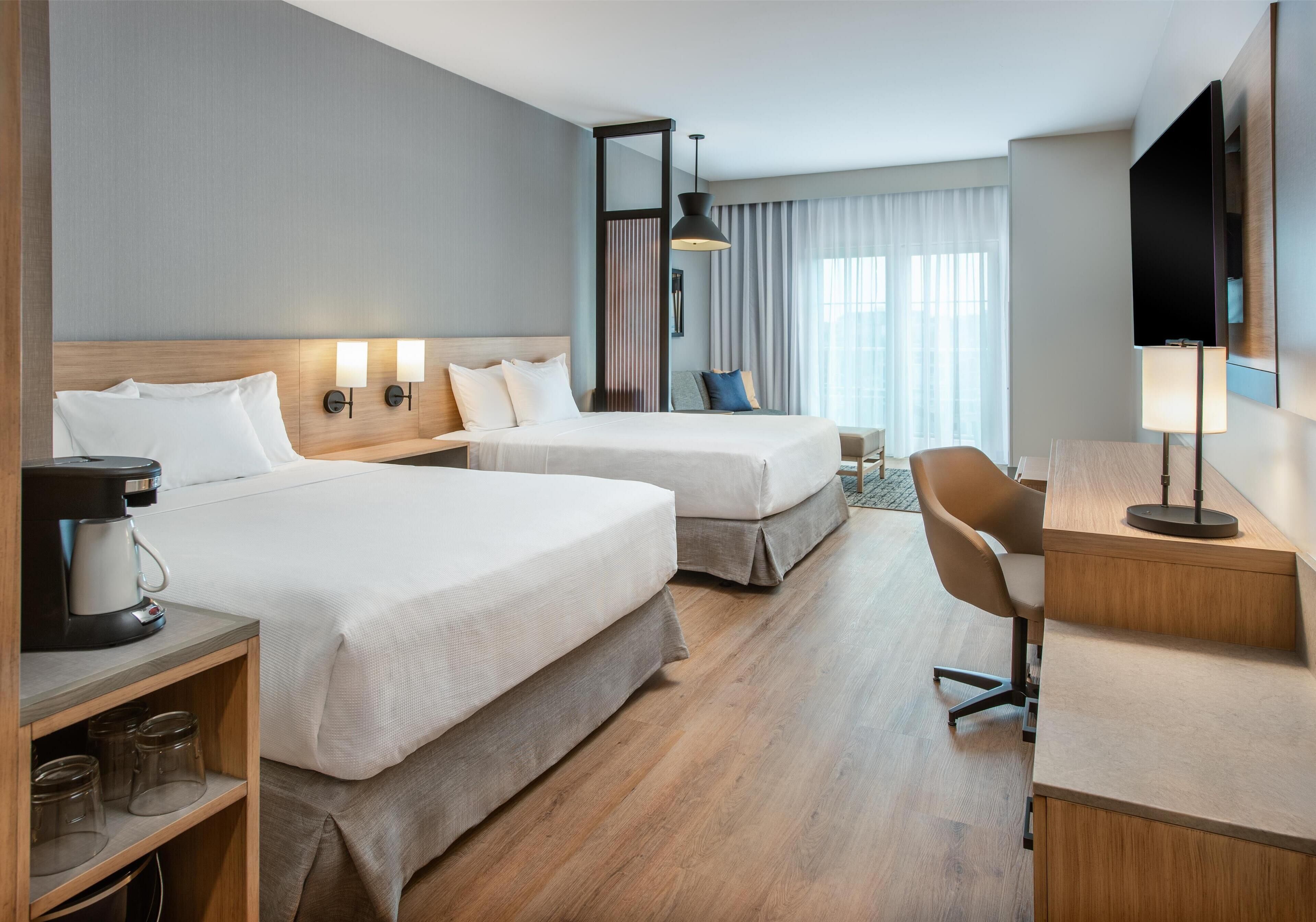 Ett hotellrum med två sängar, ett skrivbord, en stol, en kaffebryggare och en TV.