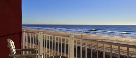 Una terraza de madera con dos sillas Adirondack y una mesa, con vistas a una playa que tiene barandilla.