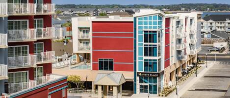 A multi-story hotel with balconies, a swimming pool, and a view of the beach.