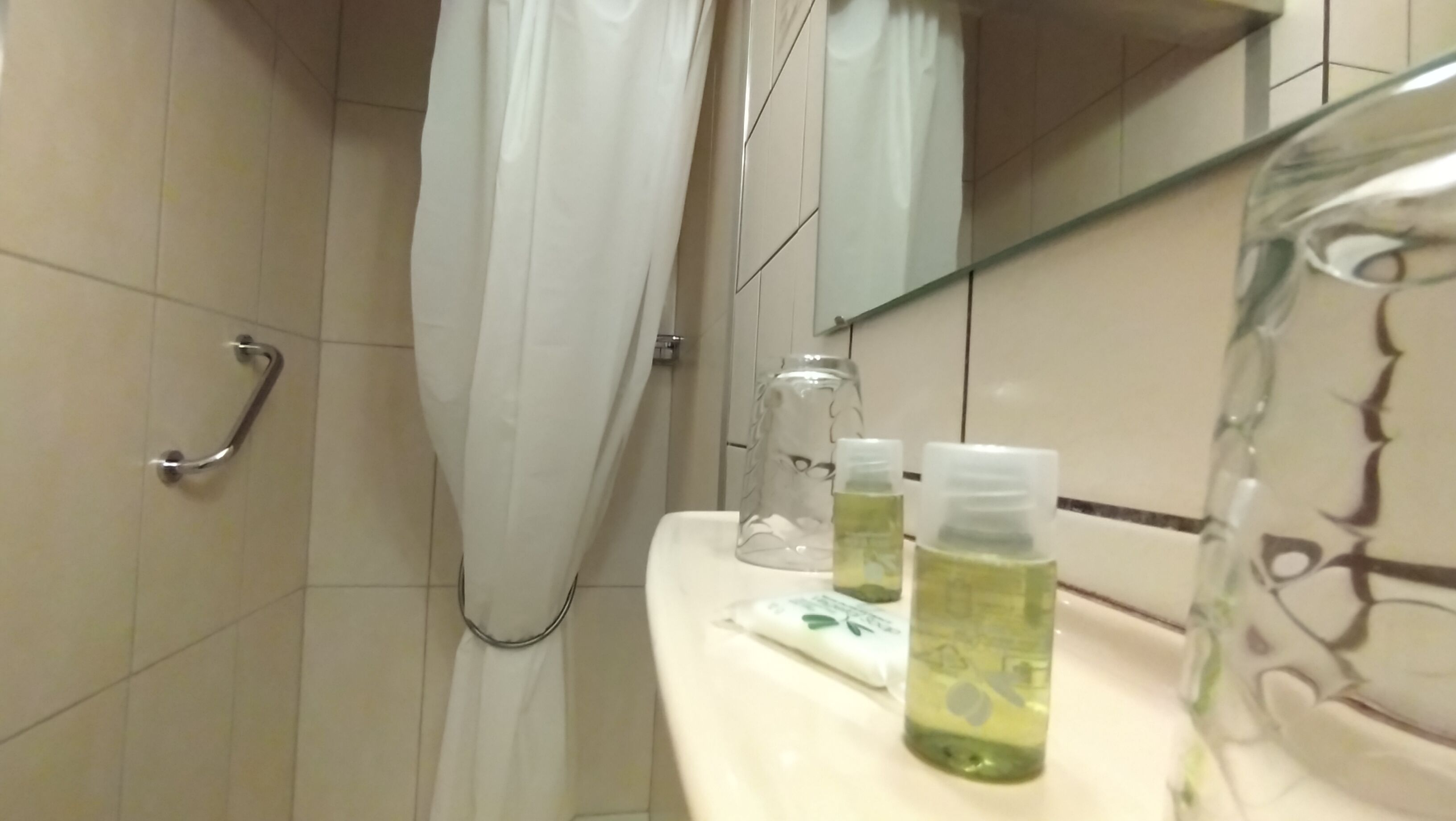 Un baño con ducha, un tarro de vidrio y dos botellas sobre el lavamanos.
