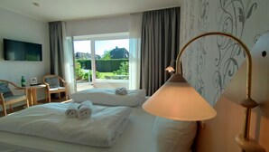 A hotel room with two beds, a TV, a table with chairs, and a view of the outdoors.