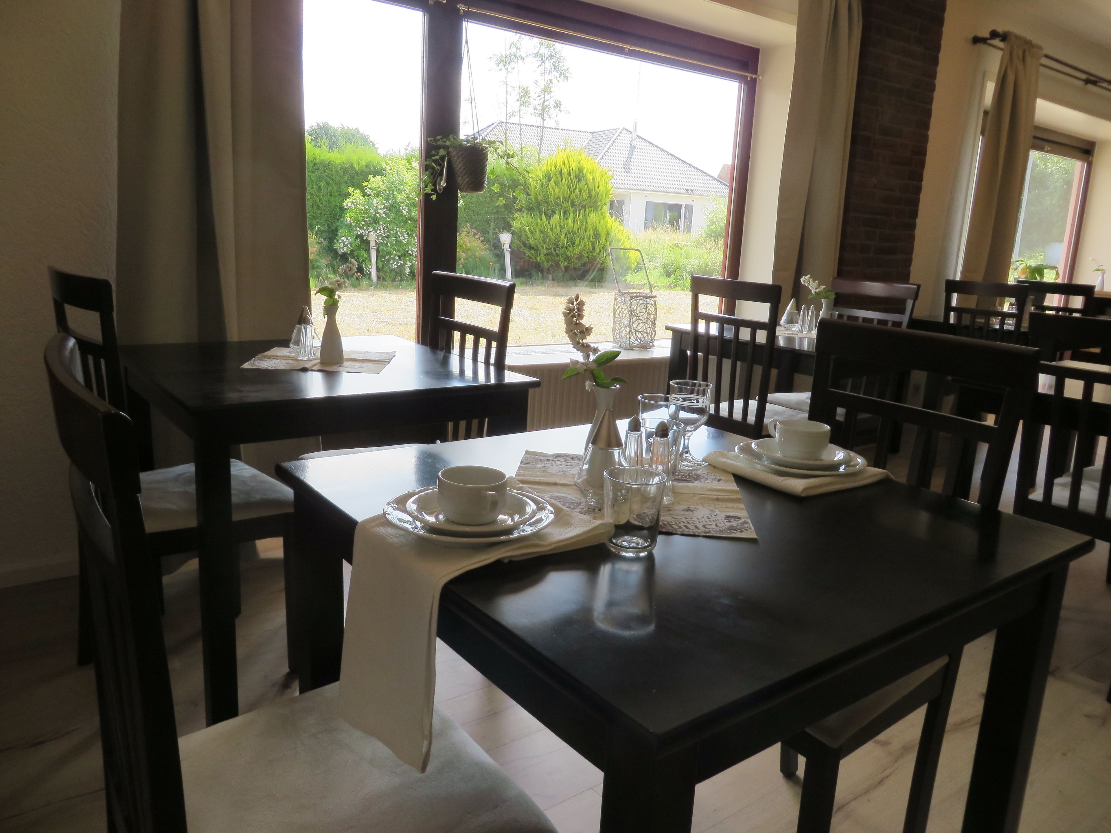 A dining area with tables set for two, featuring white tablecloths, clear glassware, and a vase with flowers.