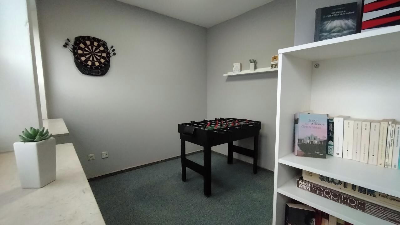 A room with a dartboard, a foosball table, a bookshelf, and a potted plant.