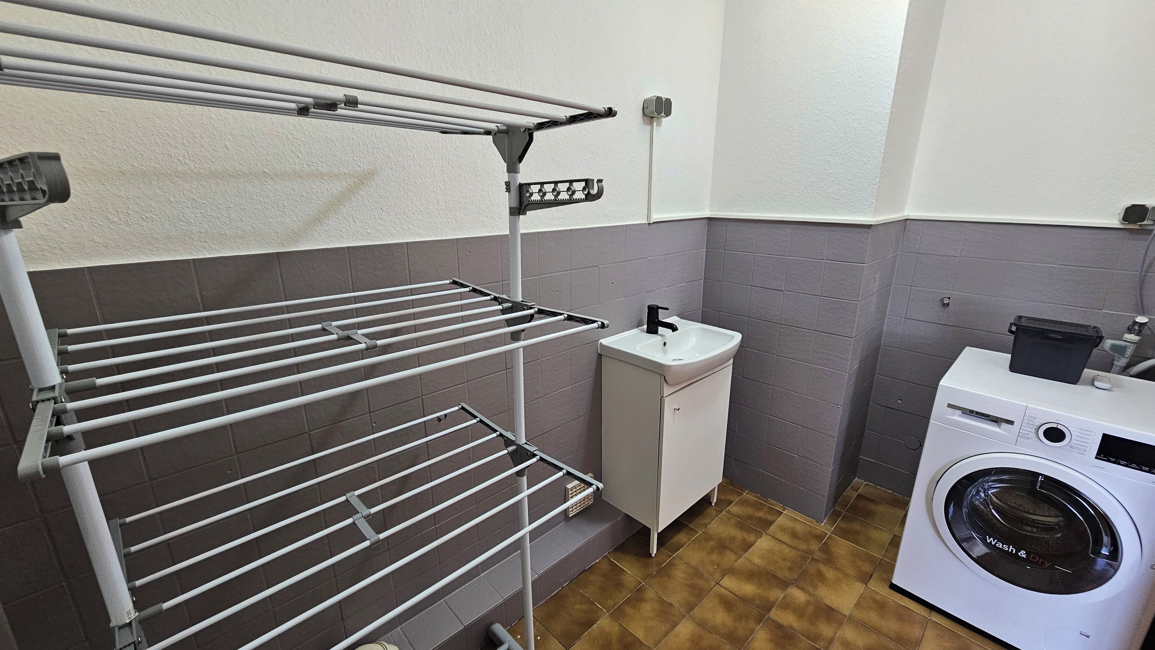 Een kleine wasruimte met een wasmachine, een spoelbak en een droogrek.