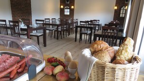 A dining area with tables and chairs, a buffet with meats, fruits, eggs, and bread.