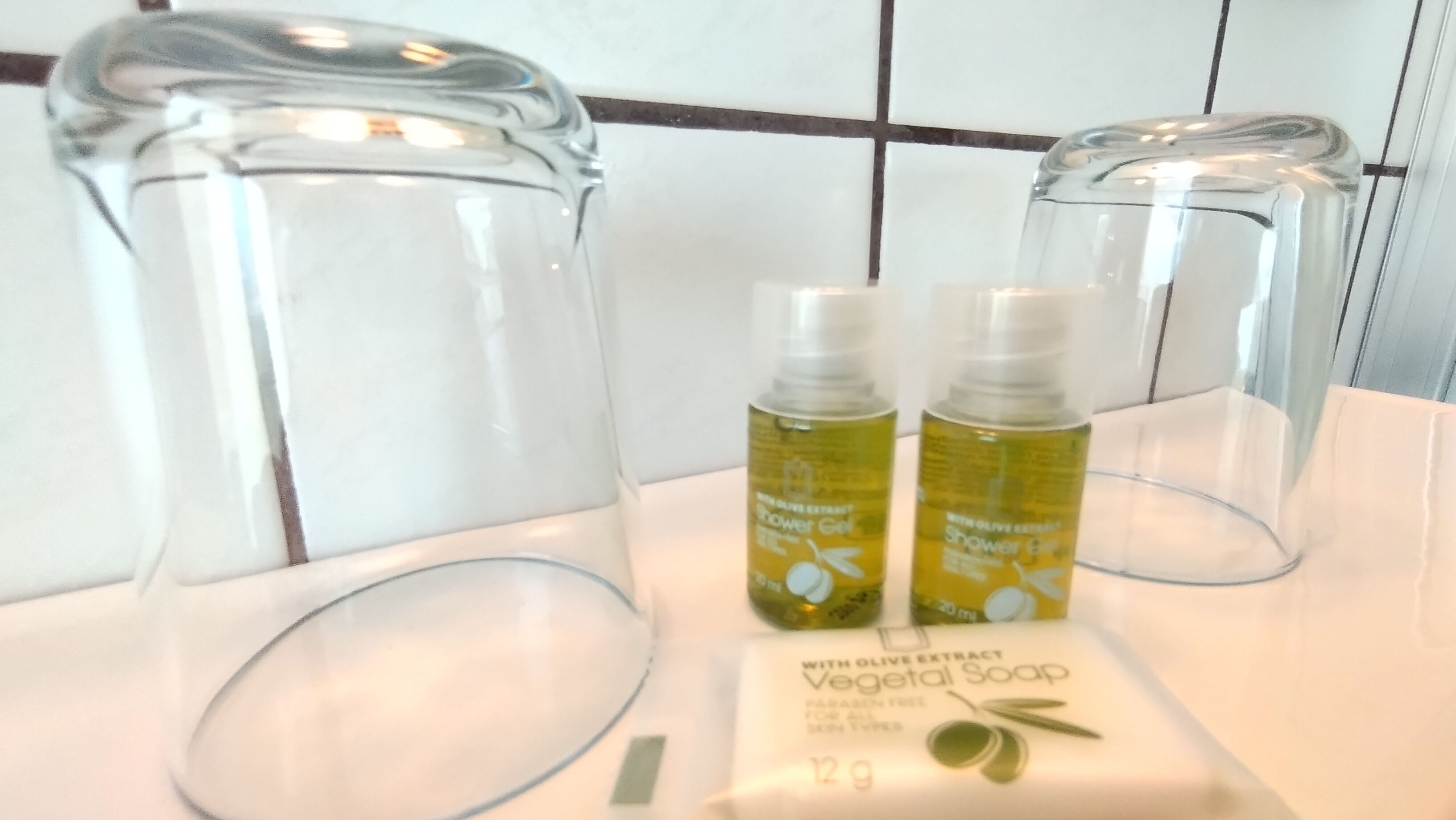 A bathroom with clear glass containers, two bottles of shower gel, and a bar of soap.