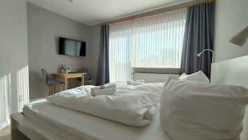 Une chambre d’hôtel comprenant un lit, un bureau, une chaise, un téléviseur fixé au mur et une fenêtre avec des rideaux.
