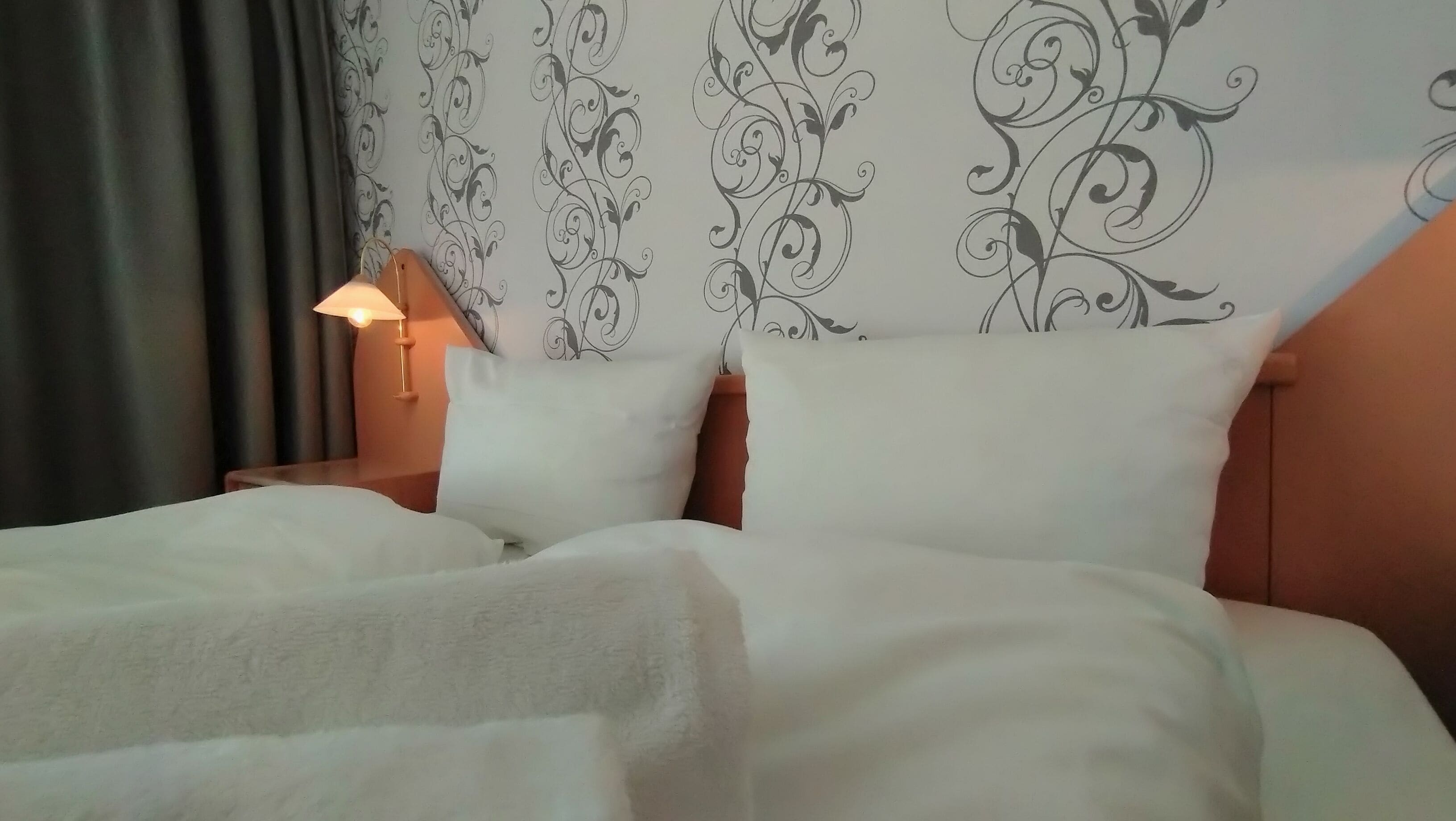 A neatly made bed with white linens, a decorative headboard with a floral pattern, and a bedside lamp.