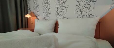 A neatly made bed with white linens, a decorative headboard with a floral pattern, and a bedside lamp.