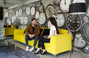 Un interior moderno con un sofá amarillo, una pared de relojes y una lámpara de pie.