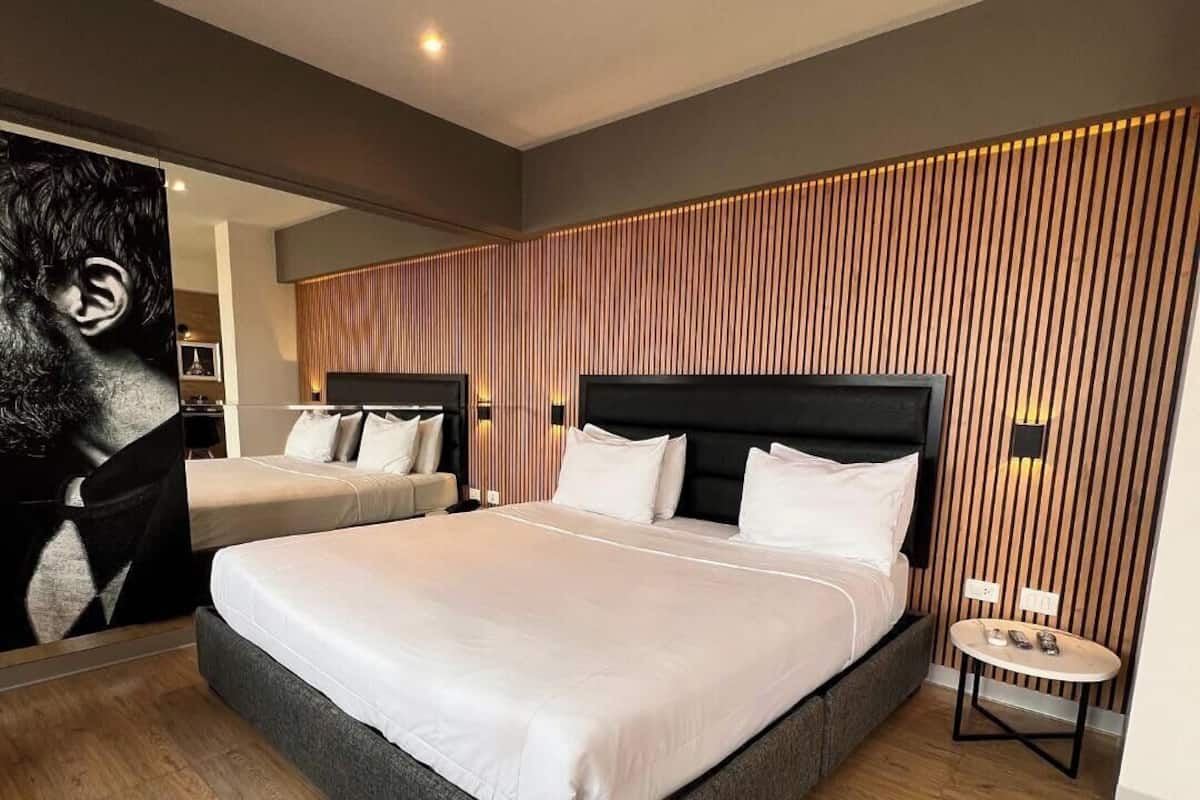 A modern hotel room with a large bed, a small bedside table, and a wooden panel wall.