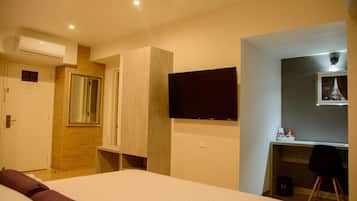 A hotel room with a bed, a desk, a chair, a television, and an air conditioning unit.