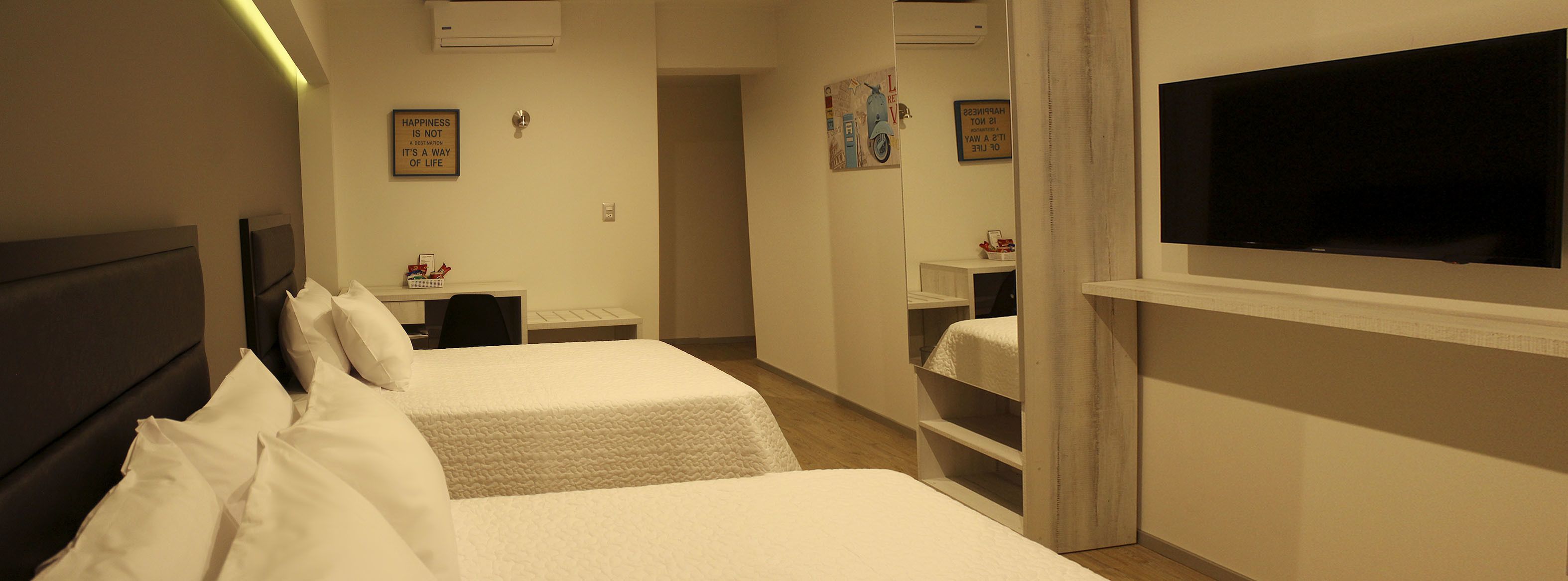 Habitación de hotel con dos camas, televisión, escritorio pequeño y estante en la pared.