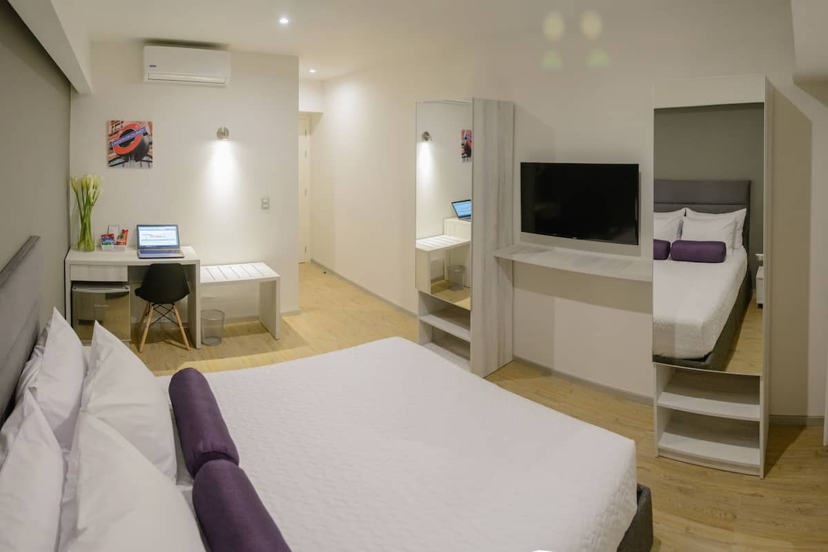 A modern hotel room with a bed, a desk with a laptop, a TV, and a wardrobe.