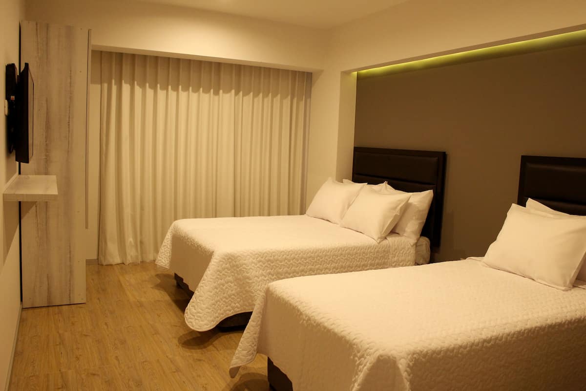 A hotel room with two single beds, a flat-screen TV mounted on the wall, and a wooden floor.