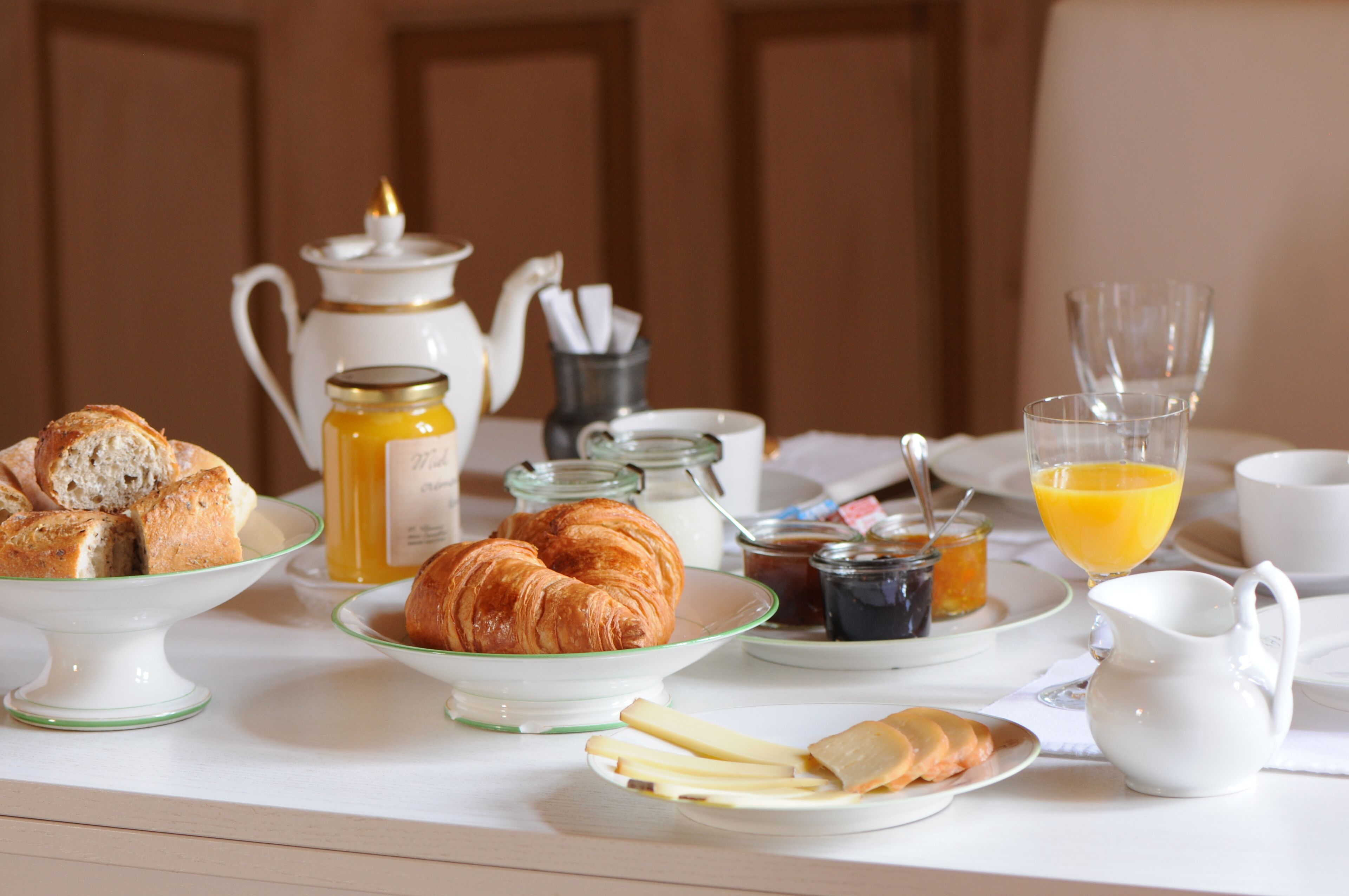Ett frukostbord med croissanter, bröd, ost och en kanna apelsinjuice.