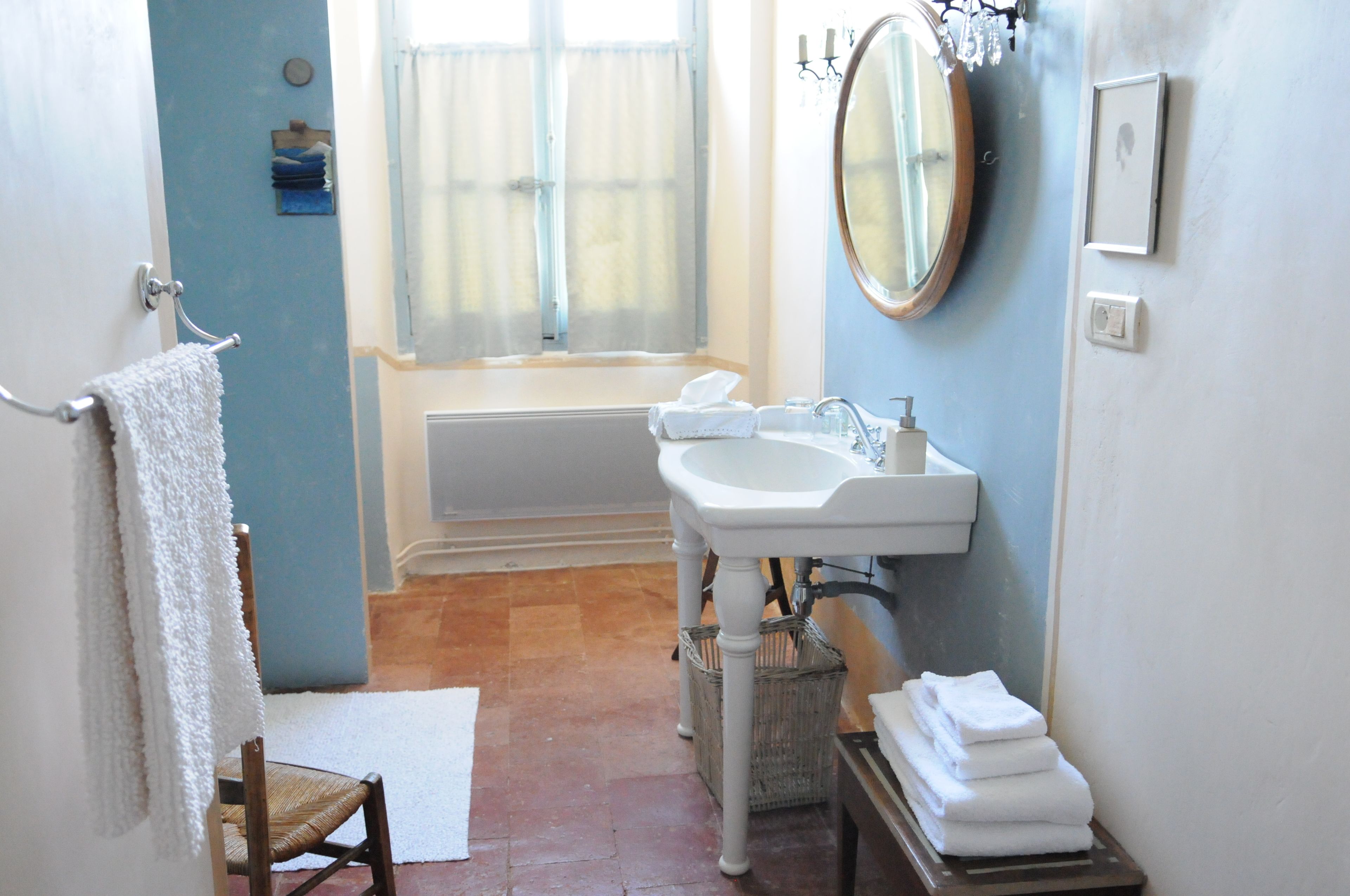 A bathroom with a bathtub, a sink, and a mirror. There is a towel rack with a towel hanging on it, and a chair is visible in the corner.