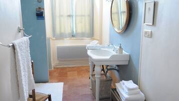 A bathroom with a bathtub, a sink, and a mirror. There is a towel rack with a towel hanging on it, and a chair is visible in the corner.