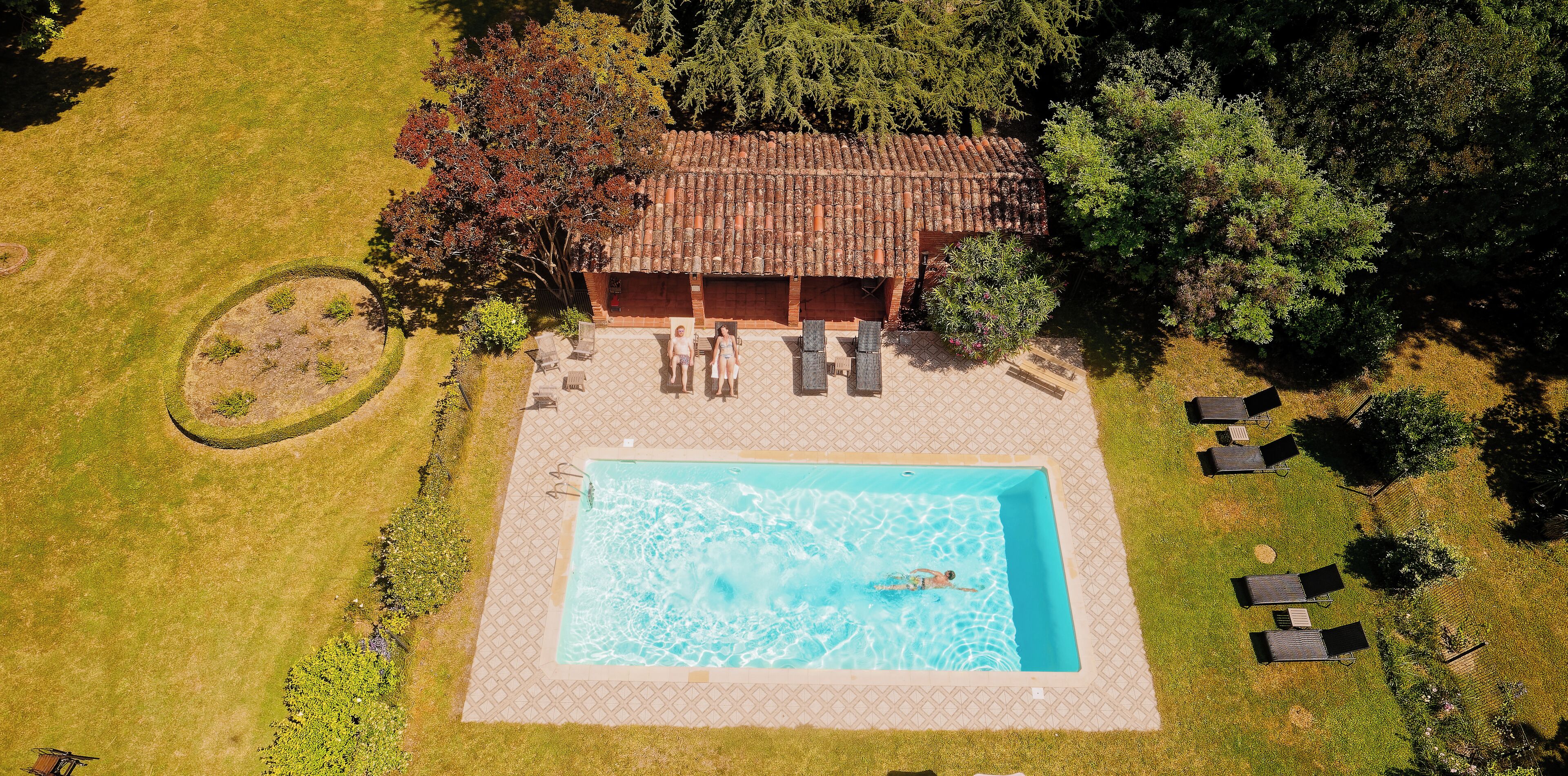 An aerial view of a property with a swimming pool, lounge chairs, and a covered patio area.
