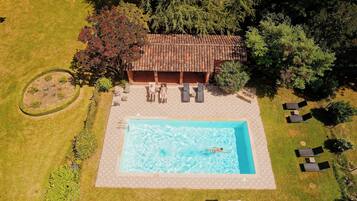 An aerial view of a property with a swimming pool, lounge chairs, and a covered patio area.