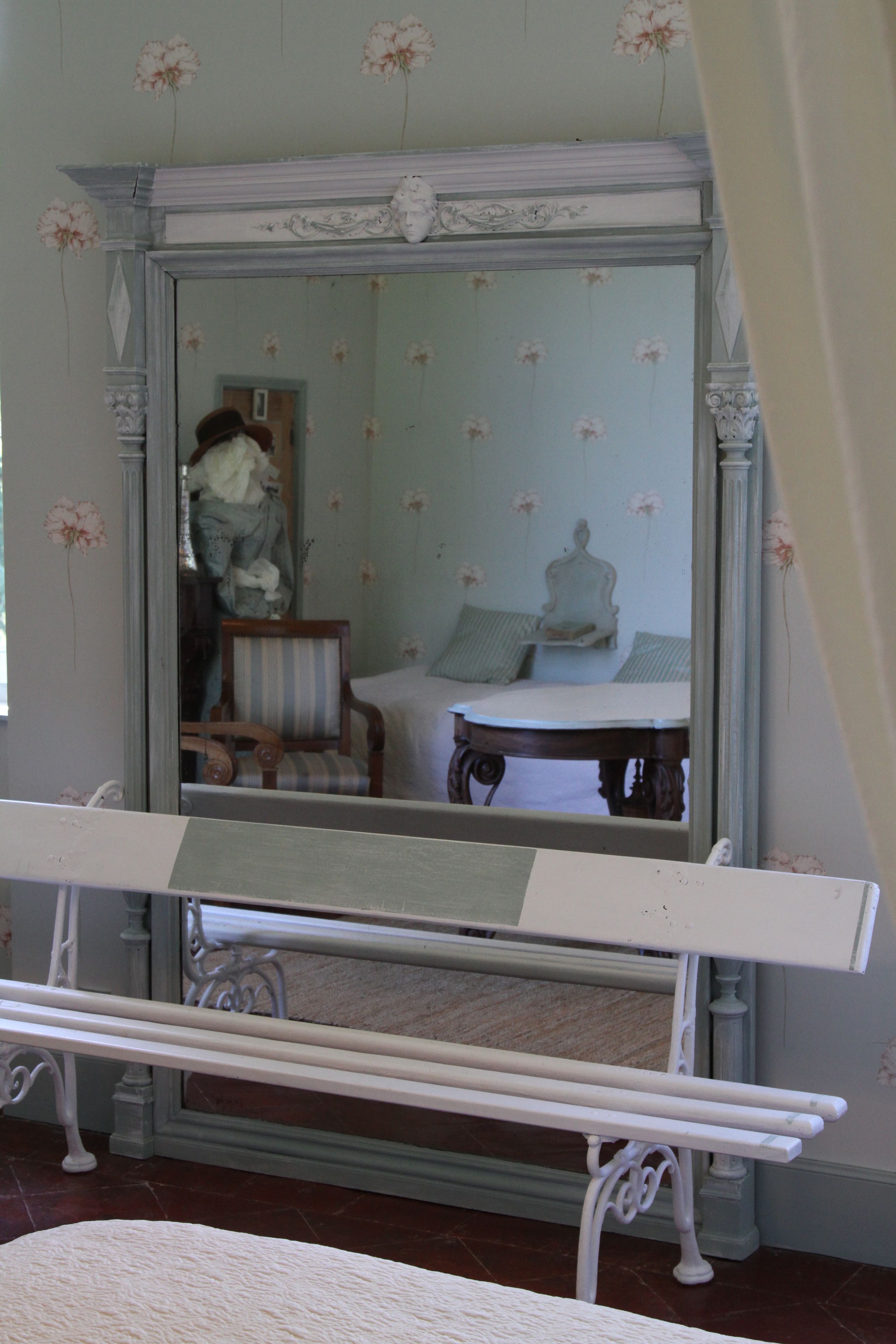 Una habitación con un espejo grande, una cama, una silla y una pequeña mesa.