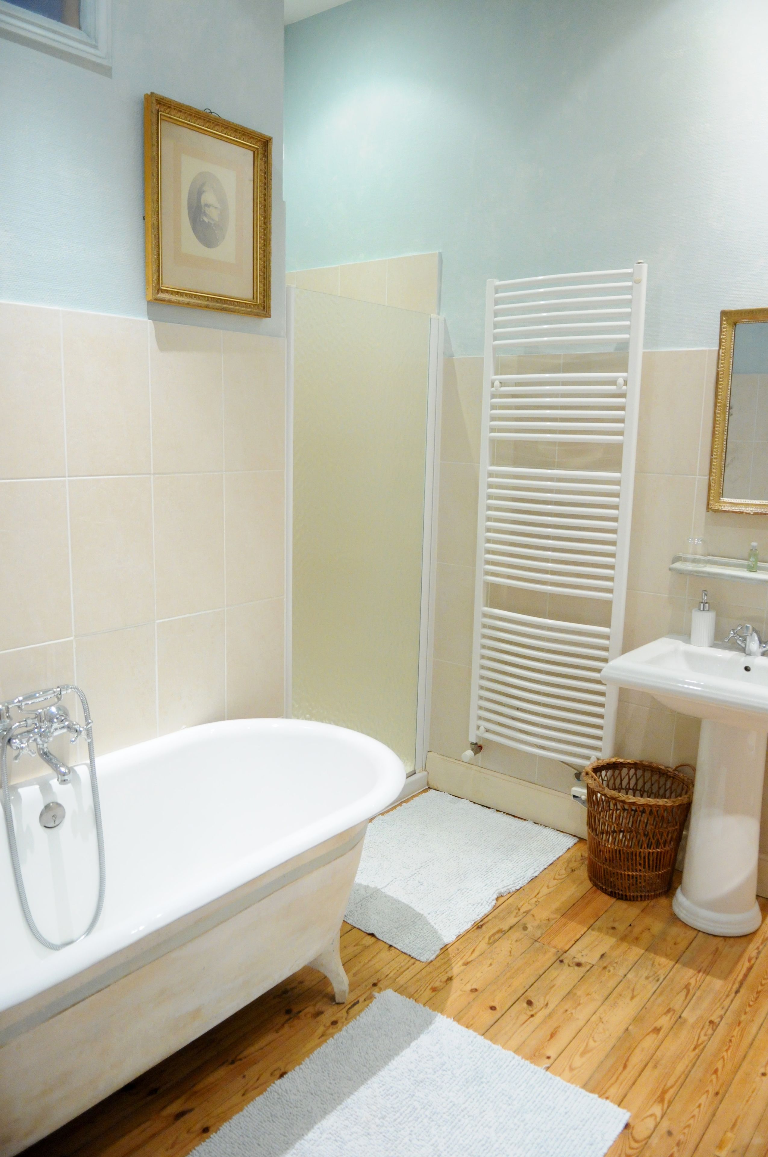 A bathroom with a white bathtub, a white sink, a white towel rack, and a framed picture on the wall.