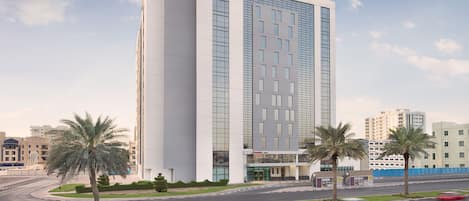 A modern hotel with a prominent 'Hampton by Hilton' sign, featuring a central entrance with a glass facade and multiple floors.