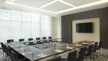 A conference room with a long table, chairs, water bottles, and a flat-screen TV on the wall.