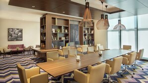 Een moderne vergaderruimte met een grote houten tafel, beige stoelen en hanglampen.