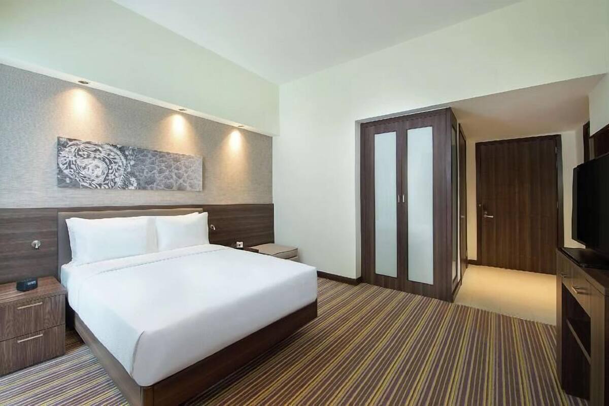 Habitación de hotel con cama, mesita de noche, televisor, armario y una obra de arte colgada en la pared.