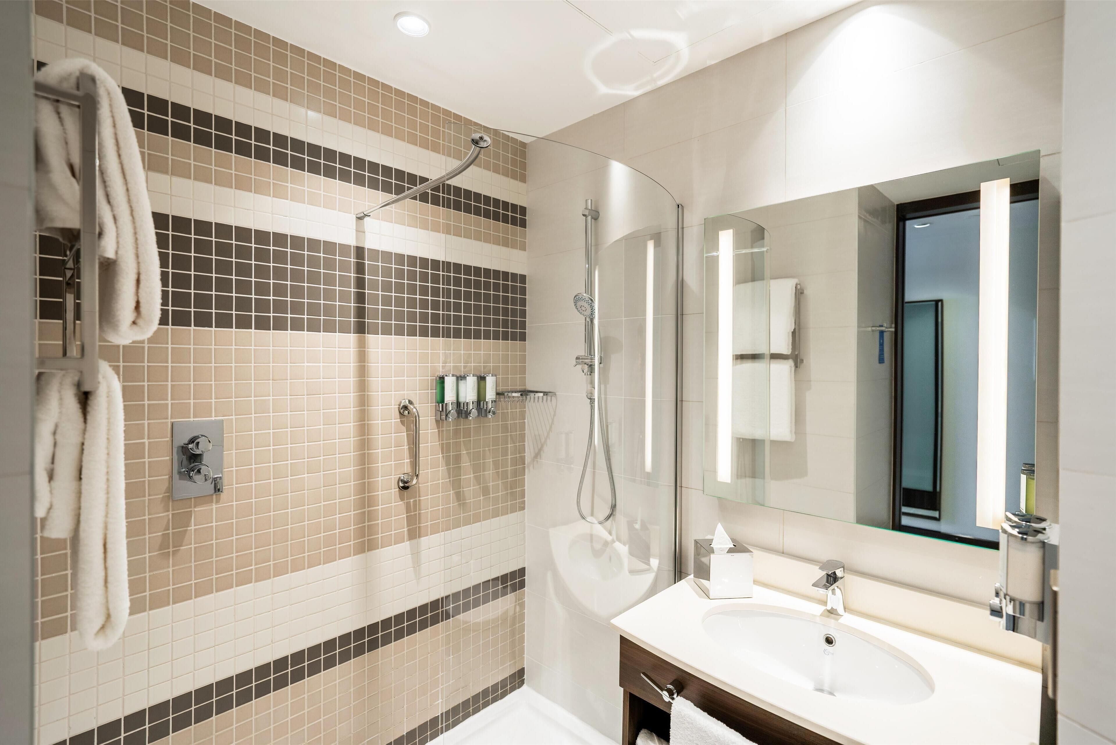 A modern bathroom with a glass shower enclosure, a large mirror, and a white sink.