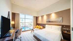 Een hotelkamer met een bed, bureau, stoel, televisie en uitzicht op een zwembad.