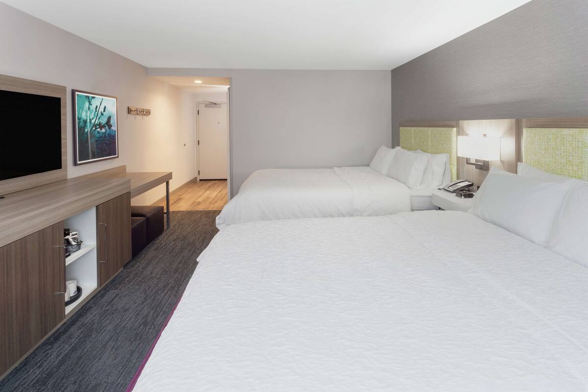 Habitación de hotel con dos camas, televisor, escritorio con lámpara y puerta que da a otra habitación.