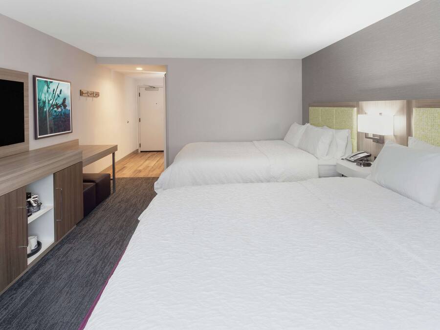 Ein Hotelzimmer mit zwei Betten, einem Fernseher, einem Schreibtisch mit Lampe und einer Tür zu einem weiteren Raum.