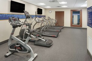 Un gimnasio con cintas de correr, elípticas y un televisor montado en la pared.