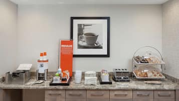 Een ontbijtbuffet met koffiezetapparaten, een koffieautomaat en een schaal gebak.
