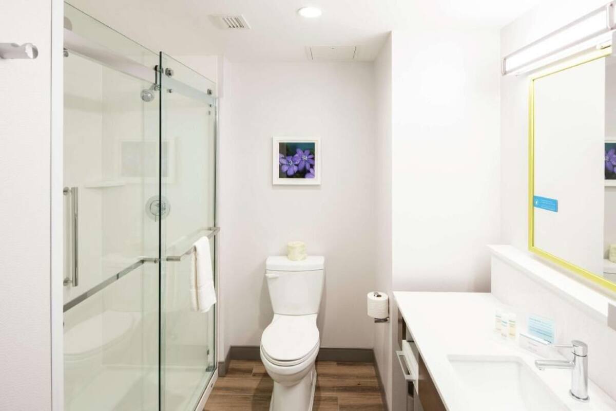 Un baño moderno con cabina de ducha de vidrio, inodoro y lavamanos blanco con espejo.