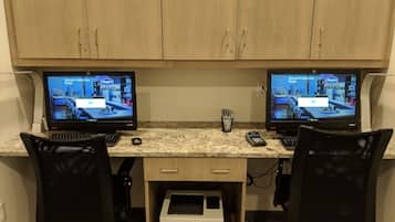 A workspace with two HP printers, two monitors, a cash register, and a coffee cup on a granite countertop.