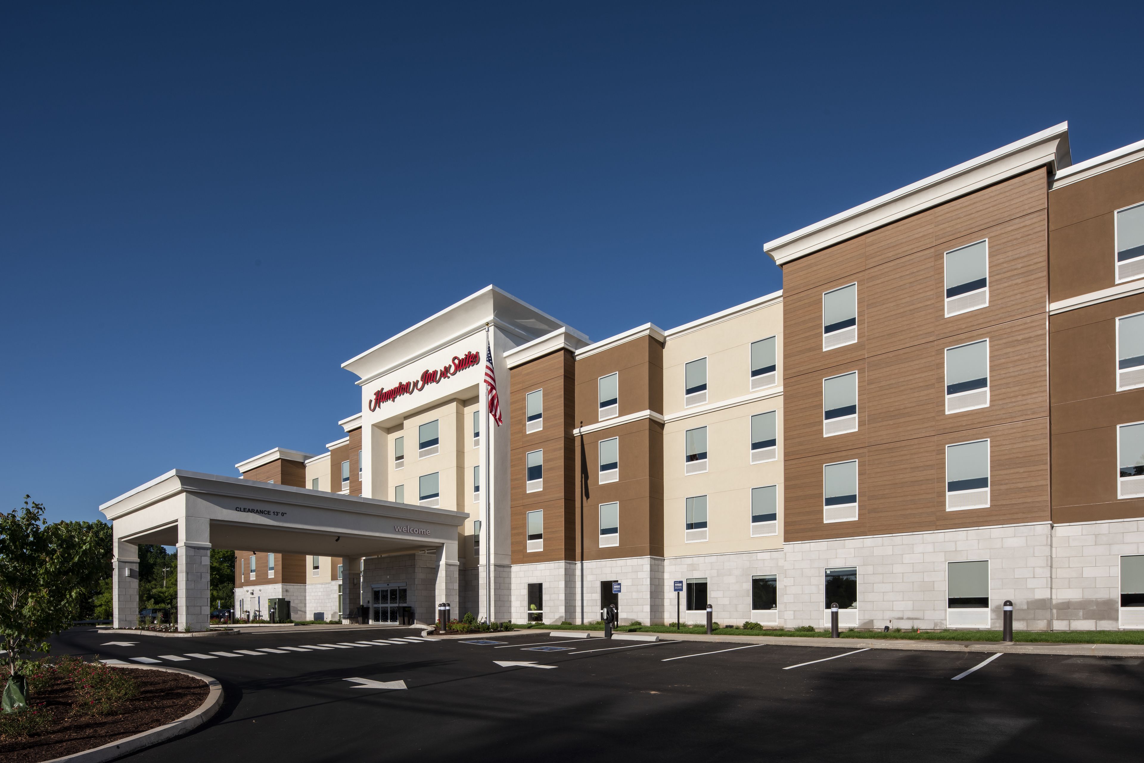 Un hôtel moderne doté d’une entrée bien visible, d’un parking couvert et d’une enseigne indiquant qu’il s’agit d’un Hampton Inn.