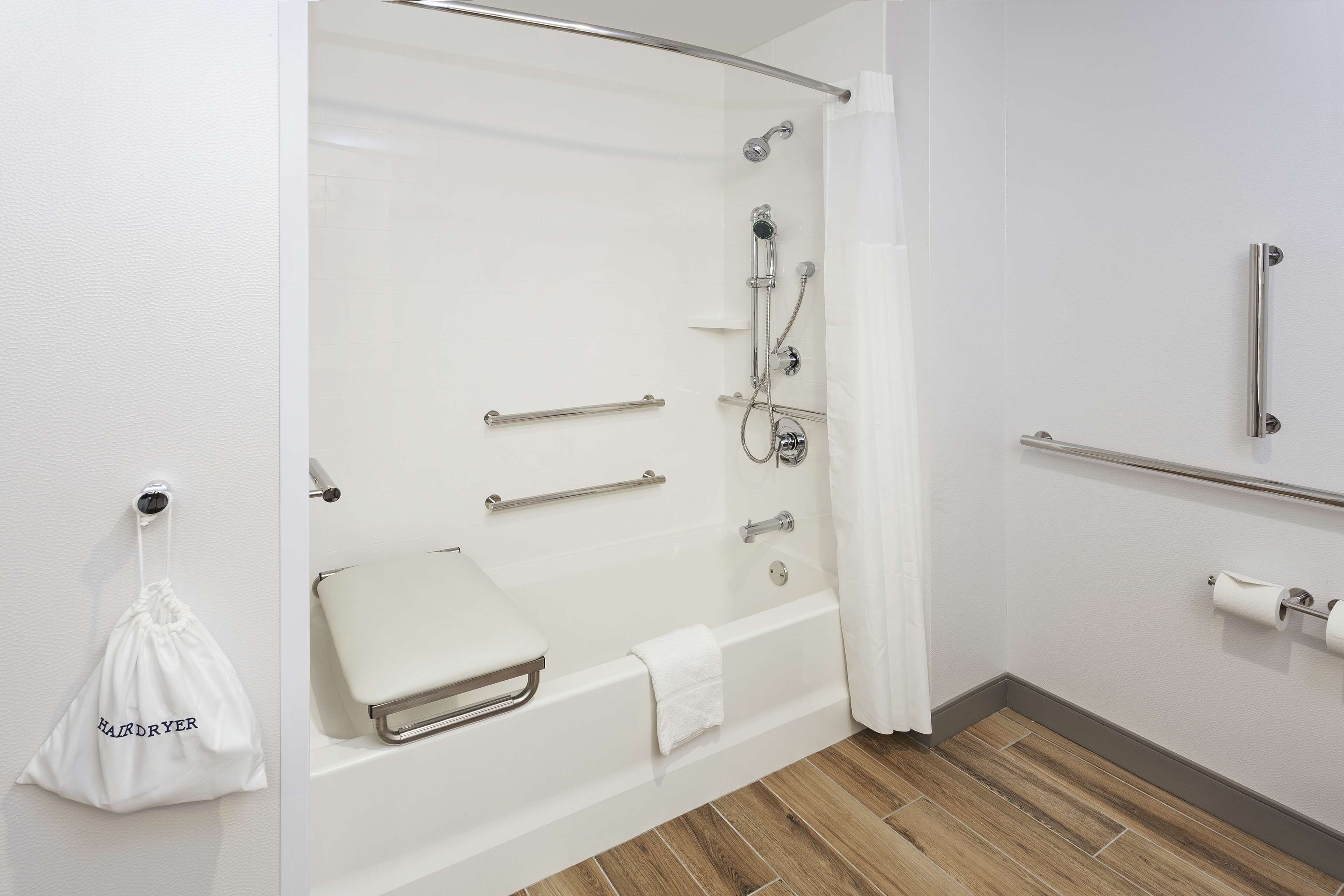 Un baño moderno con ducha a ras de suelo, barras de apoyo, un perchero para toallas y un dispensador de papel higiénico.