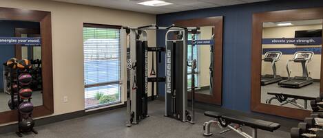 A gym with exercise equipment, a bench, and a rack of dumbbells.