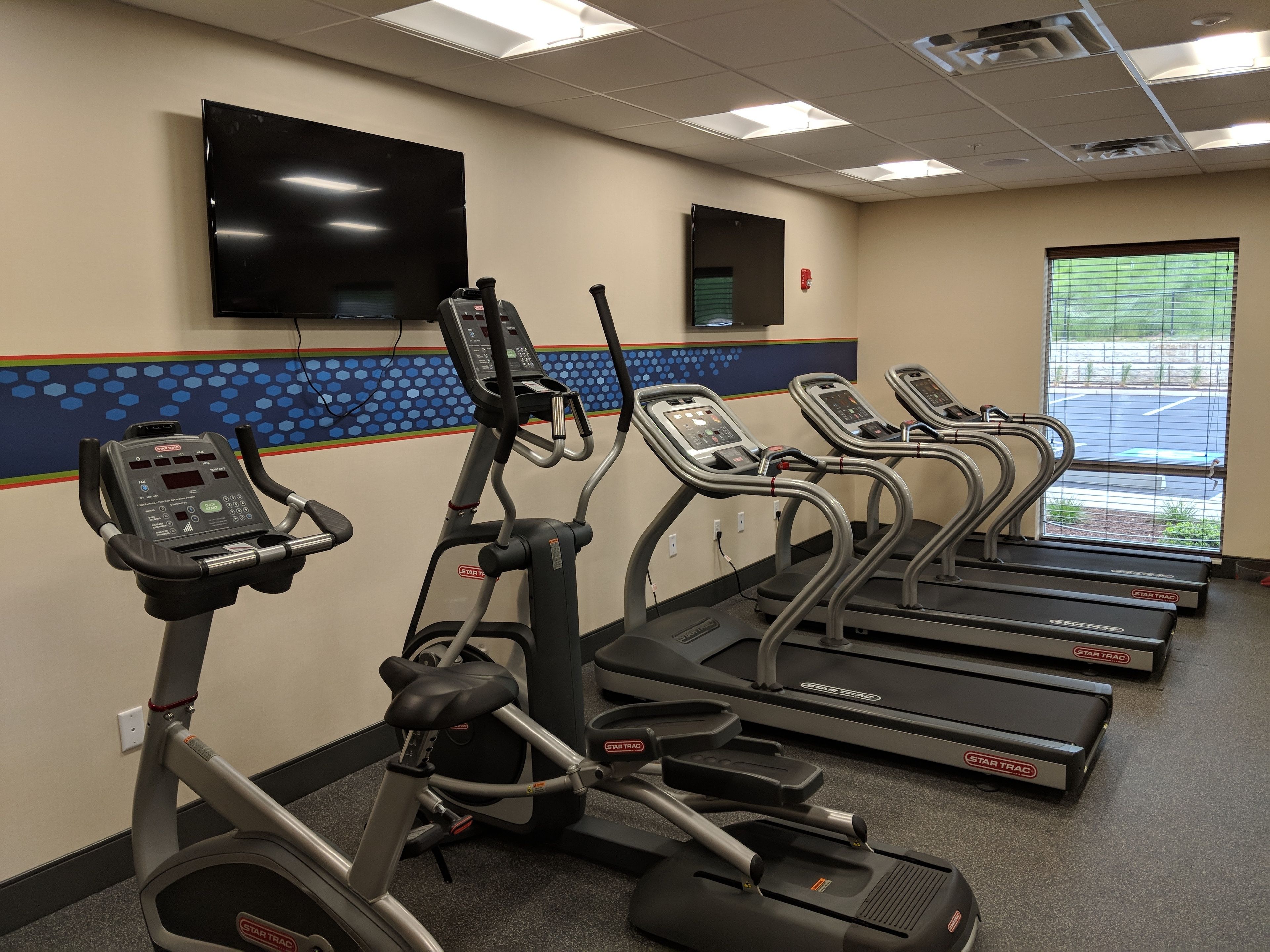 A gym with multiple treadmills, a stationary bike, and a television mounted on the wall.