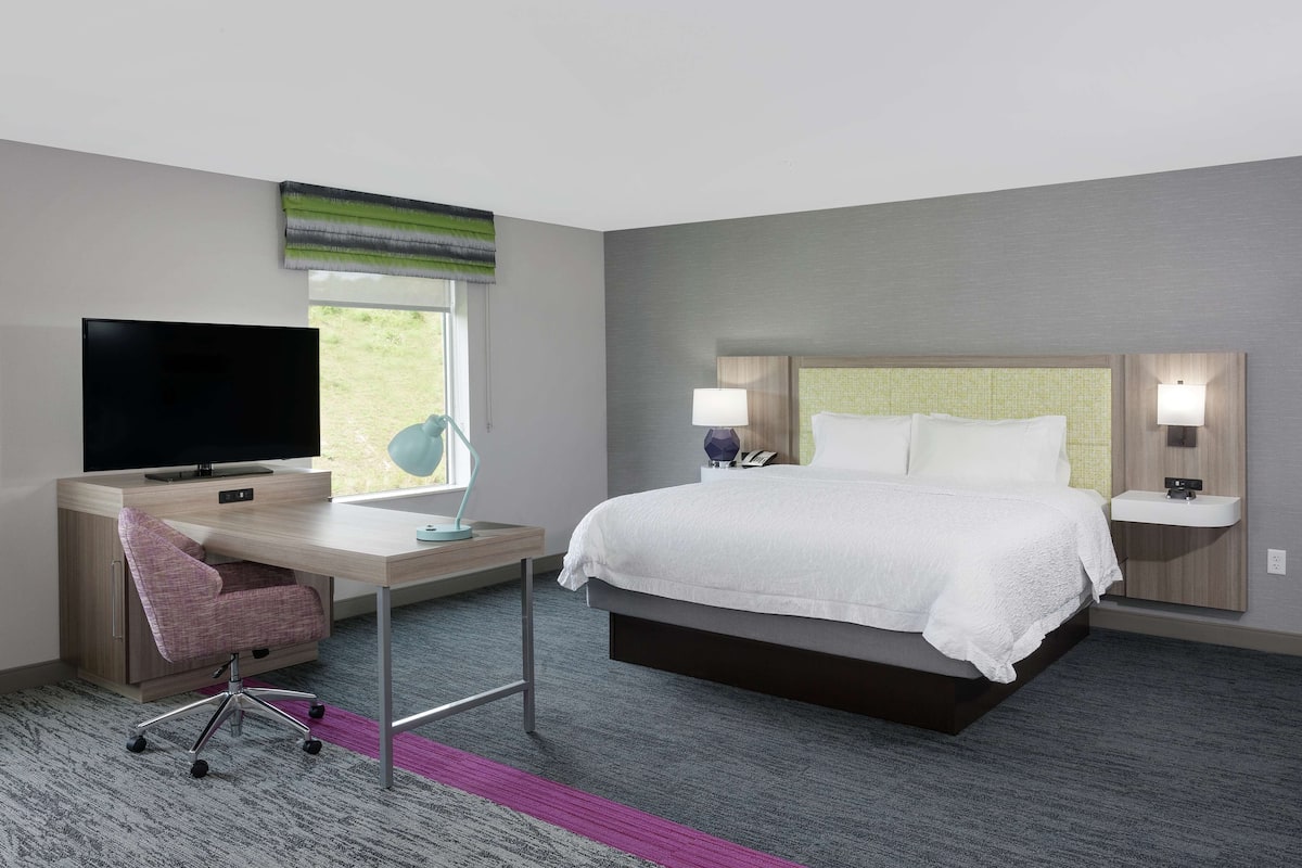Habitación de hotel con cama, escritorio con televisor, silla, ventana y mesita de noche con lámparas.